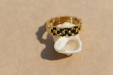 A gold-colored stainless steel ring with a linked pattern, displayed on a beige background.