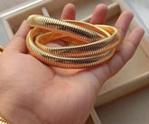 A gold-plated three-layer bracelet held in a person's hand, displaying its textured surface.