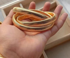 A gold-plated three-layer bracelet held in a person's hand, displaying its textured surface.