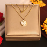 Gold necklace with a circular pendant on a beige box, surrounded by flowers.