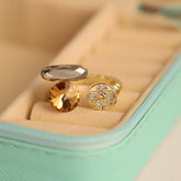 Gold ring with a large gemstone and a smaller diamond-studded design on a soft surface.