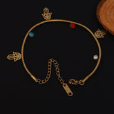 Gold bracelet with gemstones and hand-shaped charms on a dark background