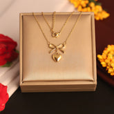 Gold necklace with heart and bow pendant in a box, surrounded by flowers