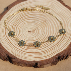 A gold-colored bracelet with floral charms displayed on a wooden slice.