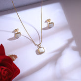 Jewelry set with necklace and earrings on a white surface with a red rose.