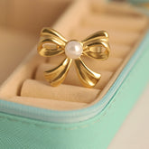 Gold bow-shaped earring with a pearl center in a jewelry box.