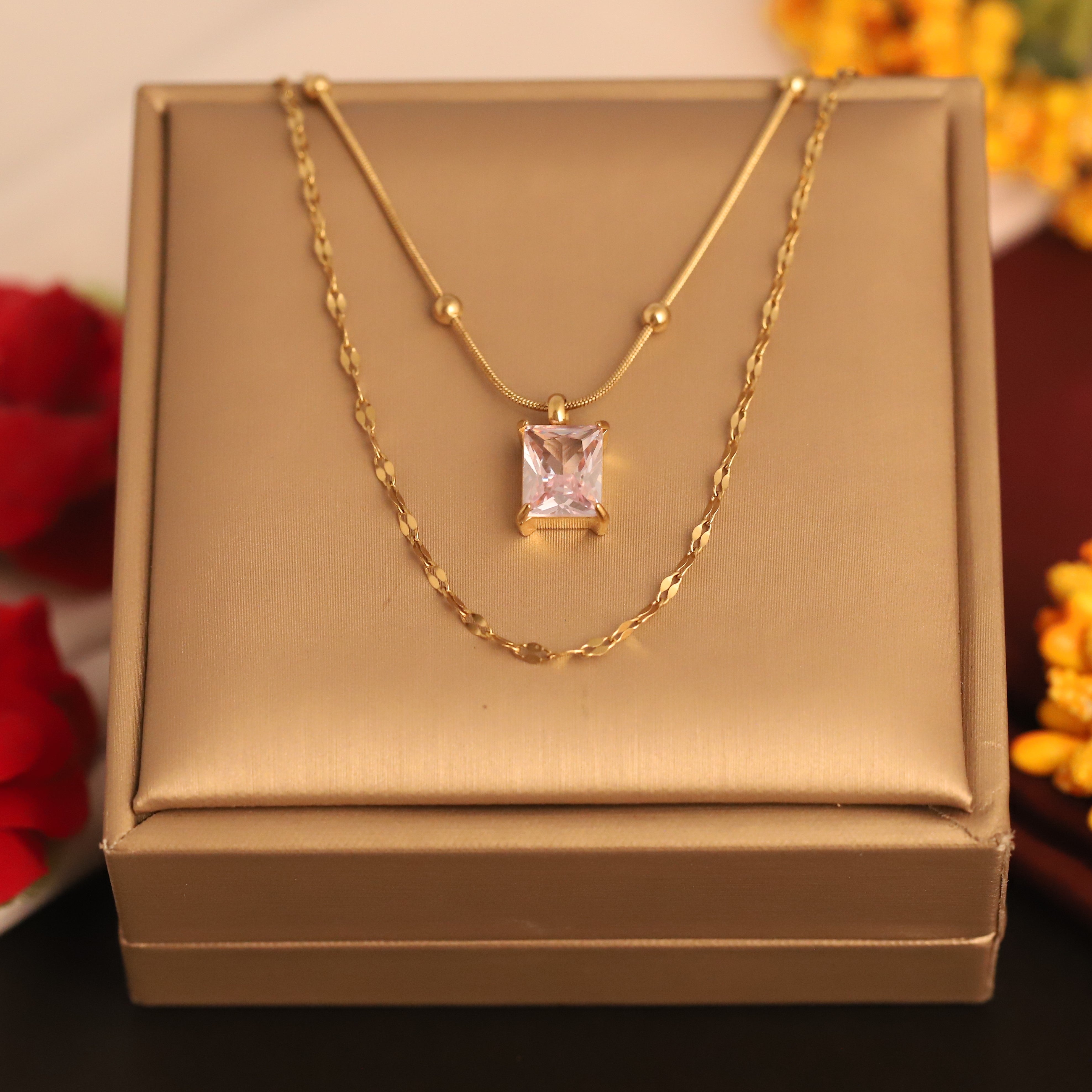 Gold necklace with a pink gemstone pendant on a gold box, with flowers in the background.