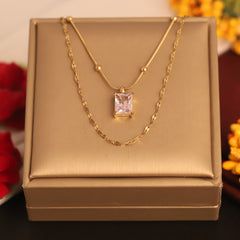 Gold necklace with a pink gemstone pendant on a gold box, with flowers in the background.