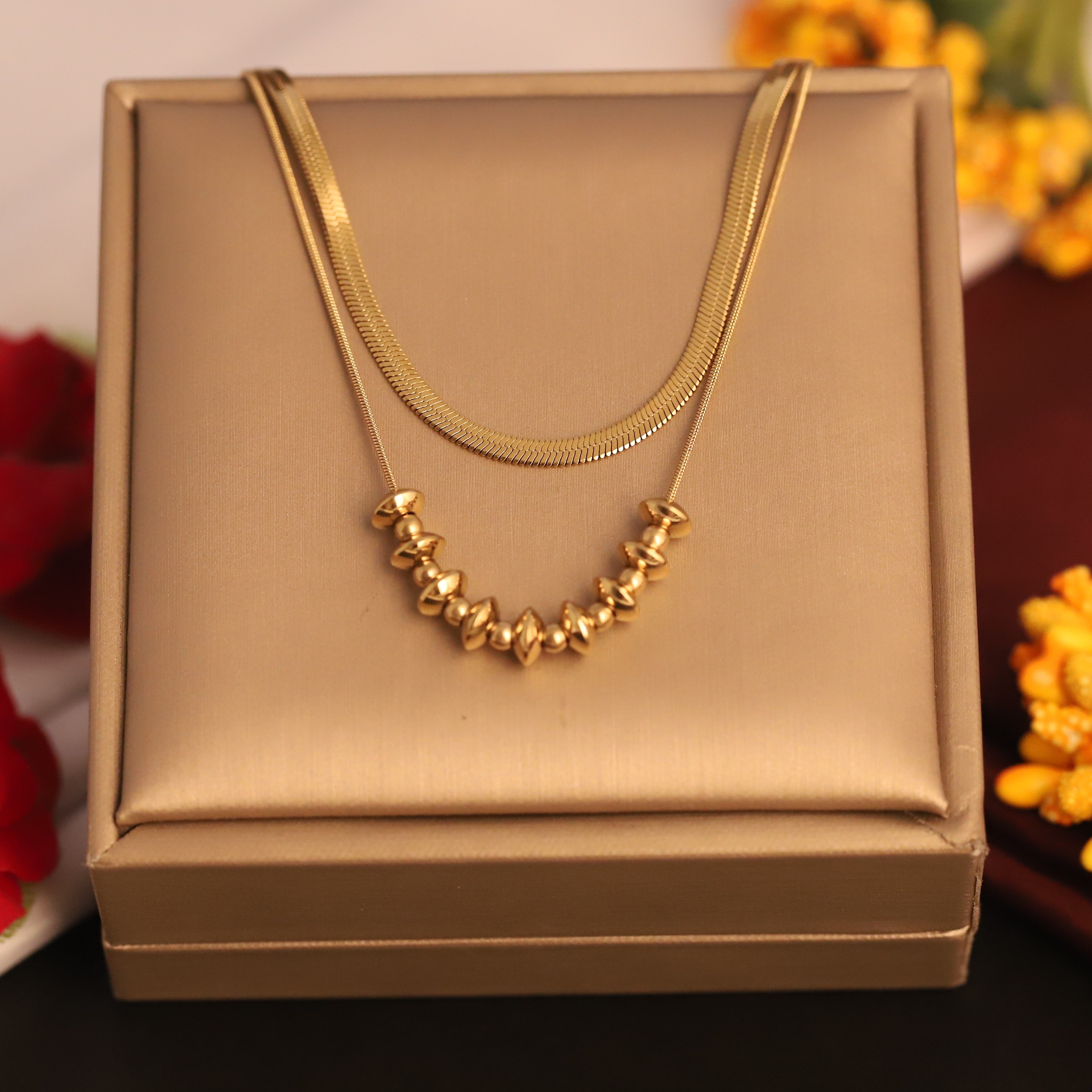 Gold necklace on a gold jewelry box with flowers in the background