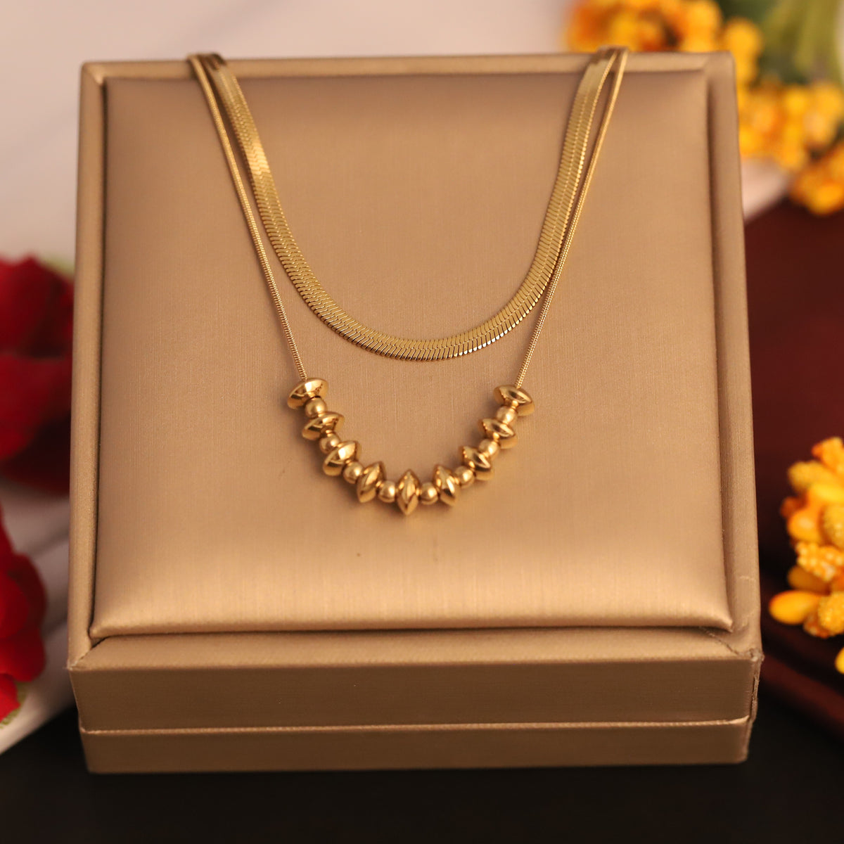 Gold necklace on a gold jewelry box with flowers in the background