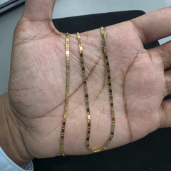 Gold chain held in a hand against a neutral background
