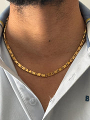 Gold chain necklace worn by a person with a light-colored shirt.