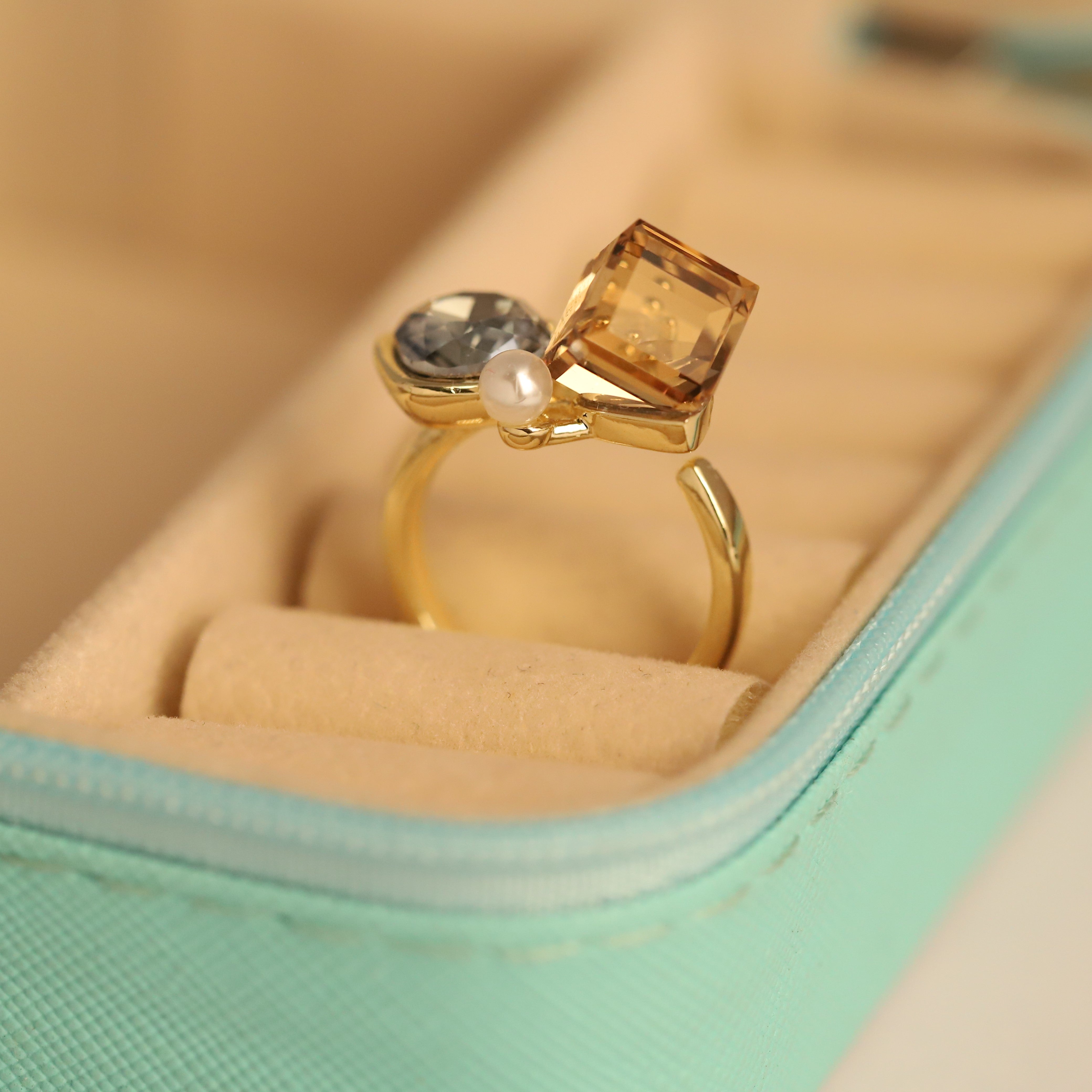 Gold ring with a square-cut gemstone and pearl on a soft surface