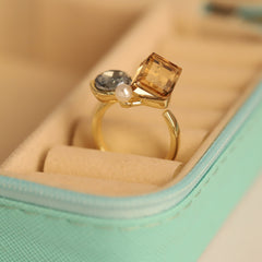 Gold ring with a square-cut gemstone and pearl on a soft surface