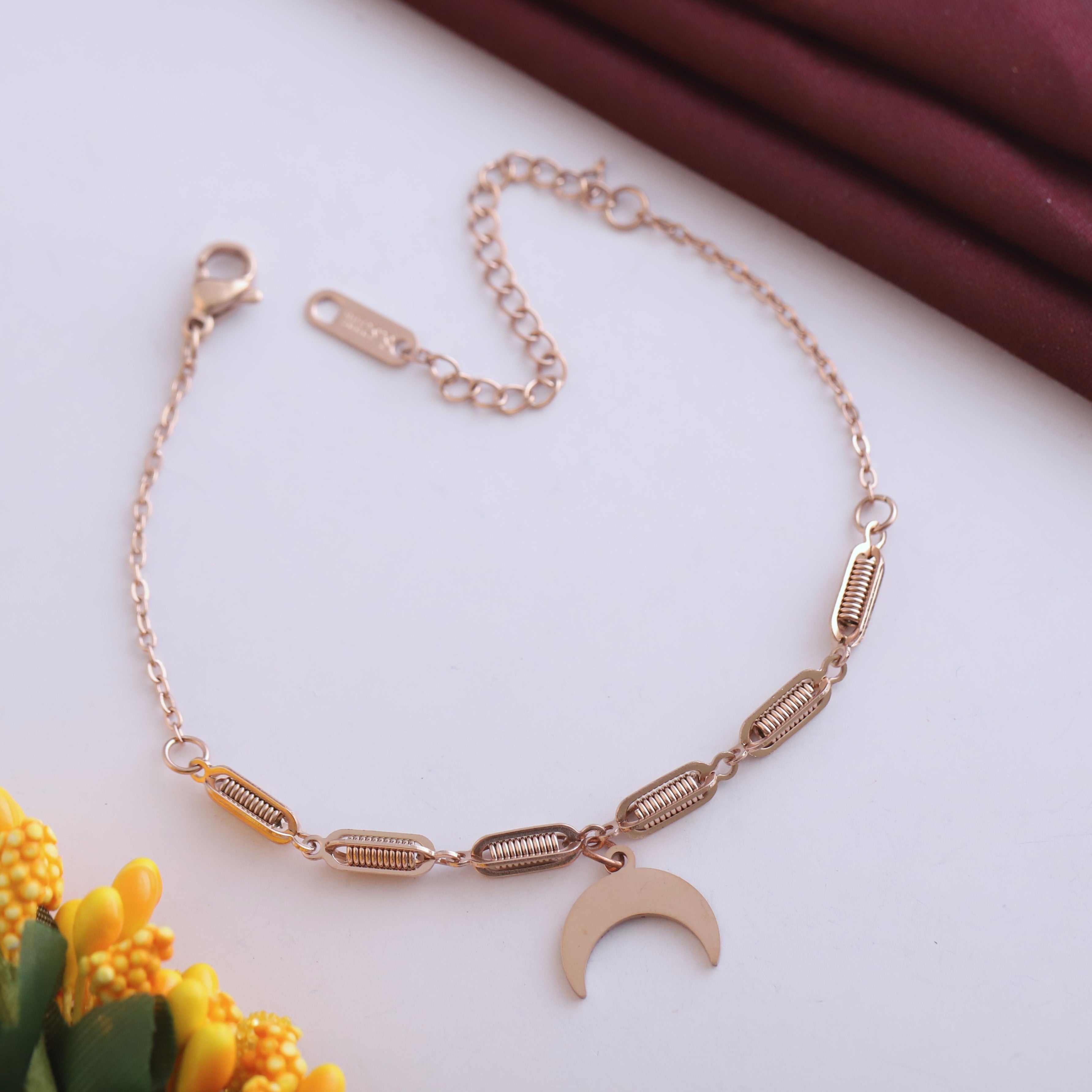 Rose gold bracelet with a moon charm on a light background